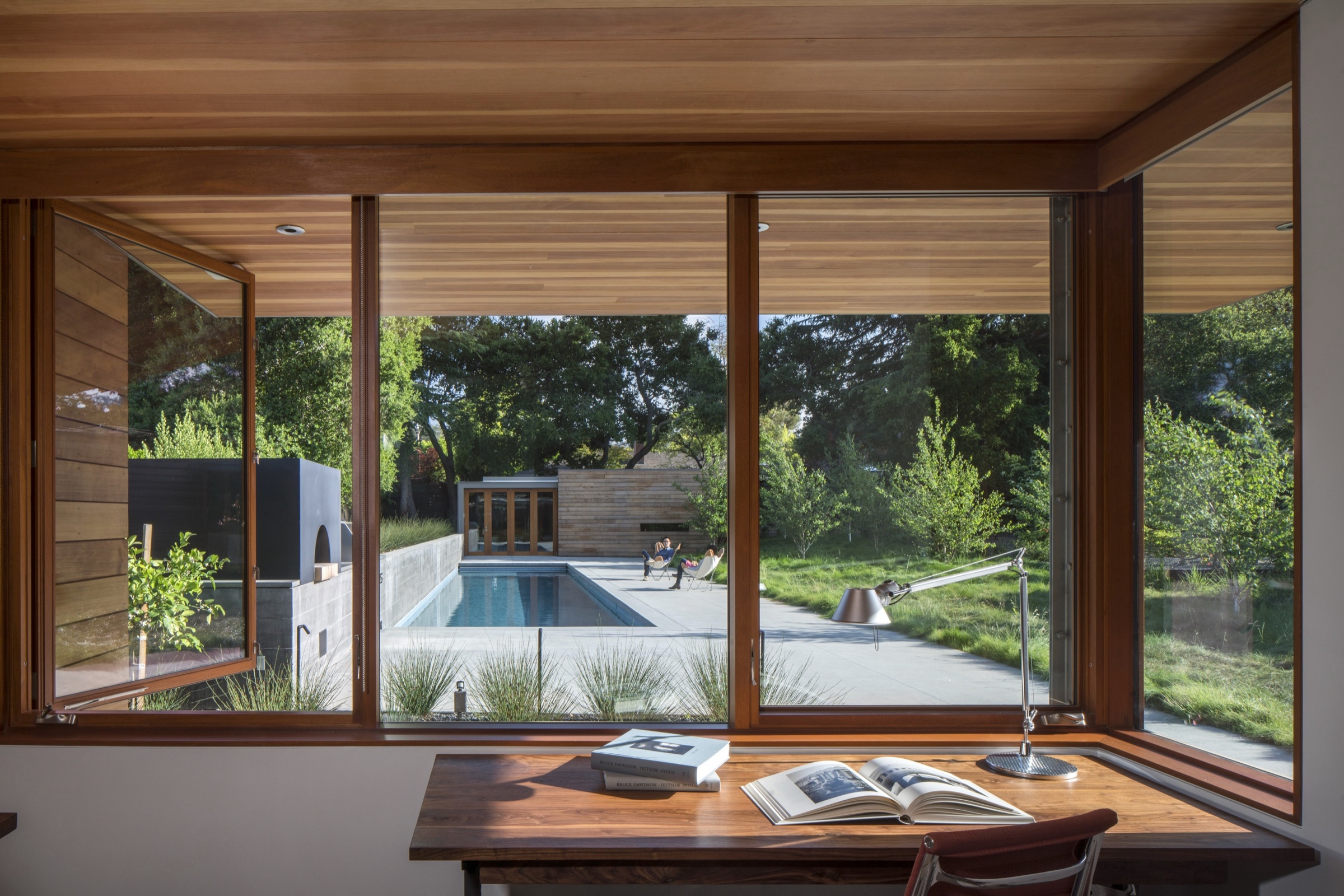 Timber-lined workspace overlooking a pool and garden